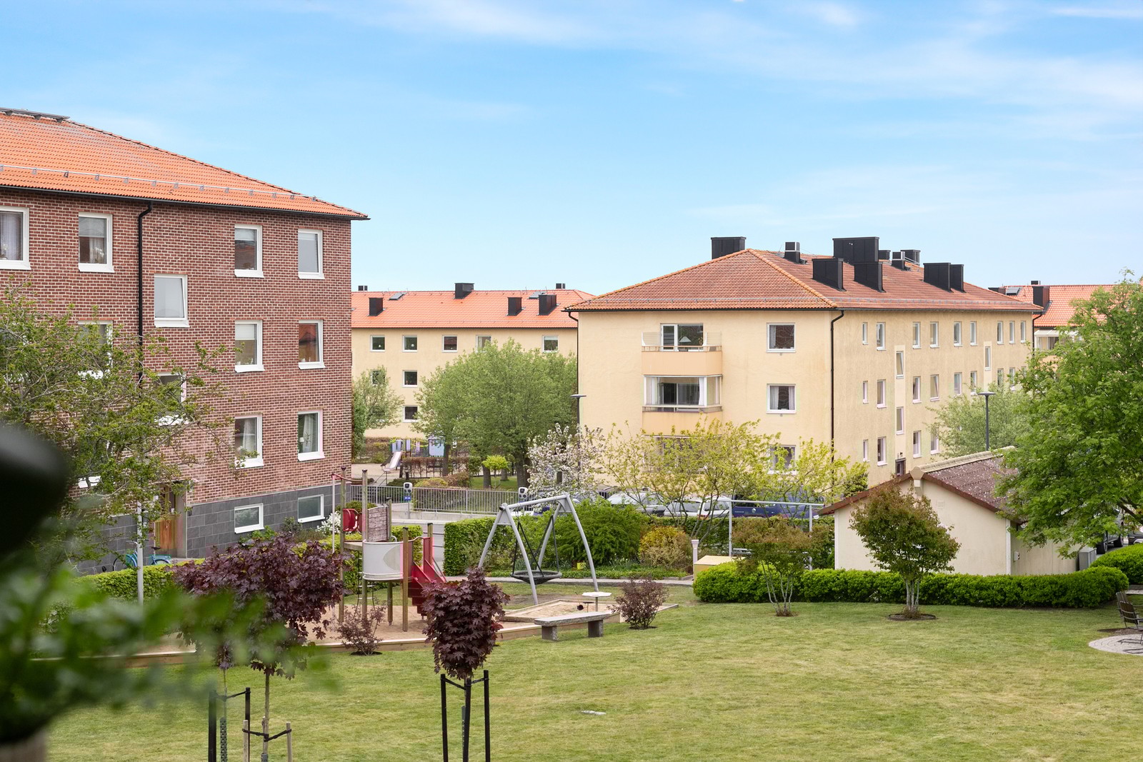 Utsikt mot grönskande innergård med lekplats och gemensamma grillplatser