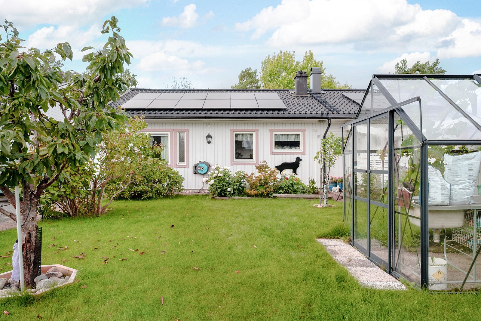 Välskött trädgård med plan gräsyta och växthus