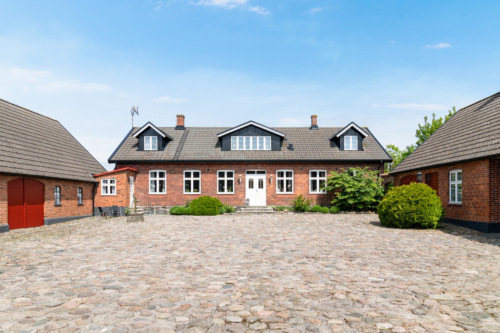 Den kullerstensbelagda gården omfamnas av boningshus och uthuslängor i tegel