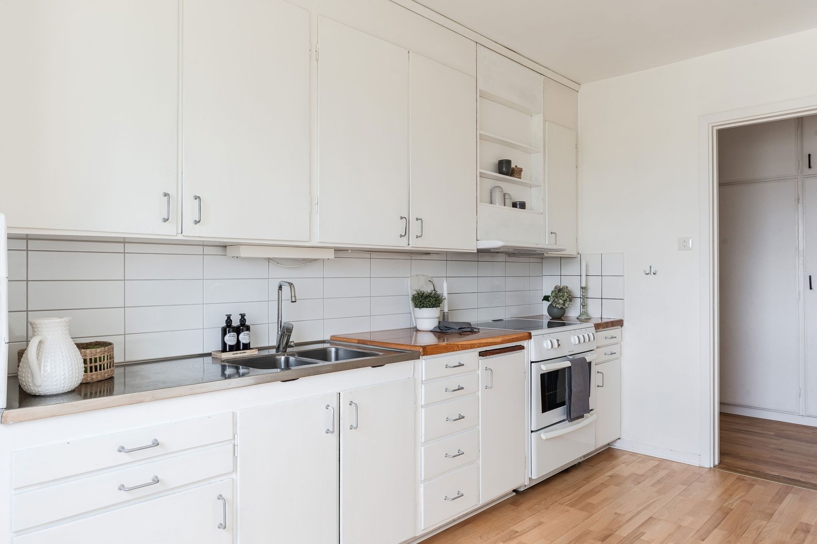 Köket är inrett med stilrena vita luckor, ljust målade väggar och ett parkettgolv