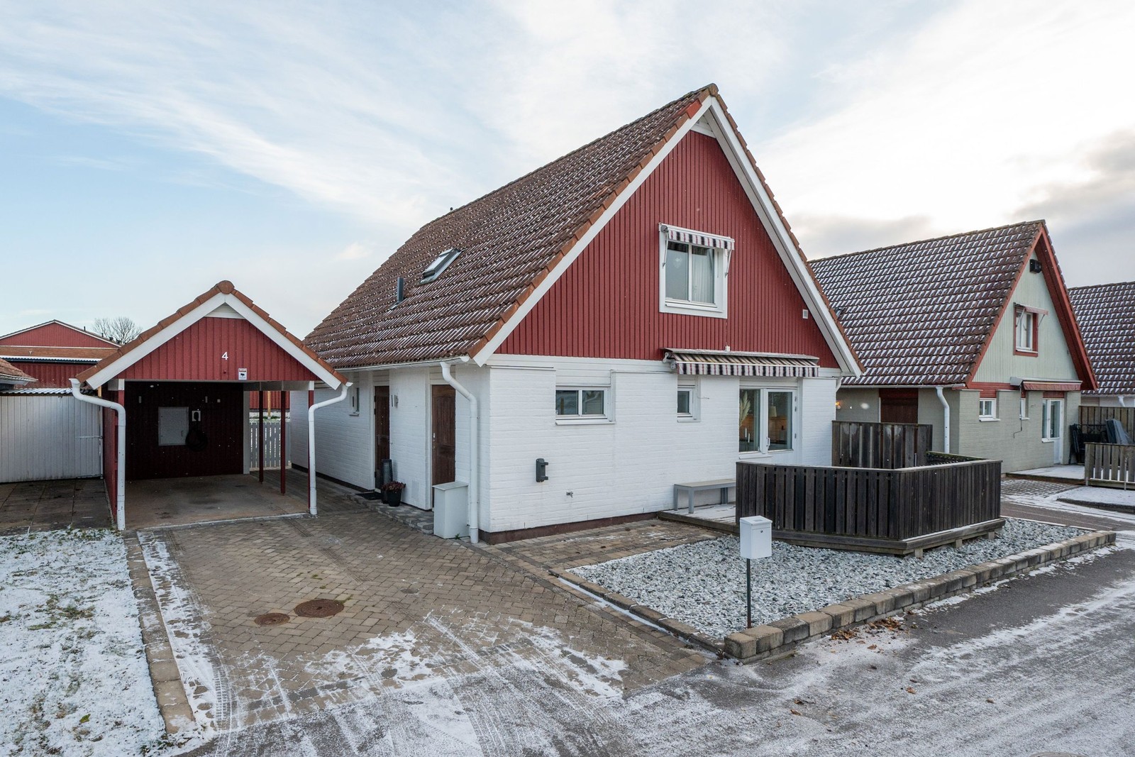 Framsida med carport, stort förråd och laddstolpe.