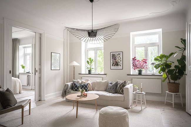 Ljust vardagsrum med stora fönster och ljusa möbler.